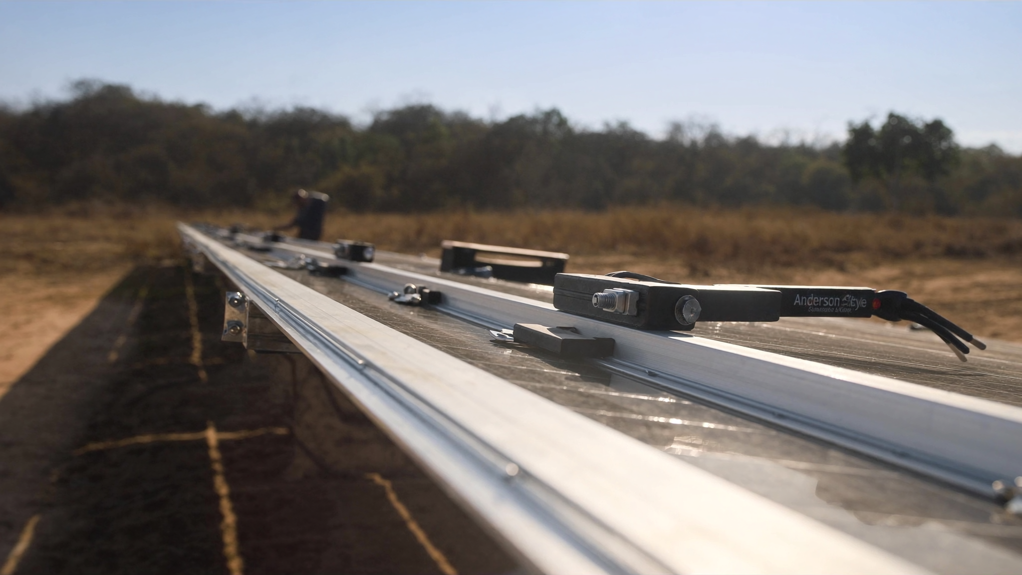 Estrutura de fixação de módulos fotovoltaicos sendo montada em campo aberto sob forte luz solar do Cerrado, com trilhos de alumínio e conectores à mostra
